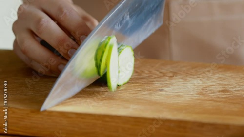 Vegetarian food. Female hands slicing fresh cucumber on wooden cutting board, close up