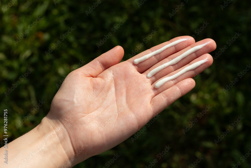 A person applying the correct amount of sunscreen for face and neck (three finger lengths).