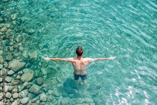 Top view of a man swimming in crystal-clear turquoise water, surrounded by smooth rocks