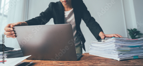 Businesswoman Overwhelmed: A close-up shot of a businesswoman struggling to manage a mountain of paperwork on her desk, captured in a candid moment of stress and pressure. The image conveys the challe photo