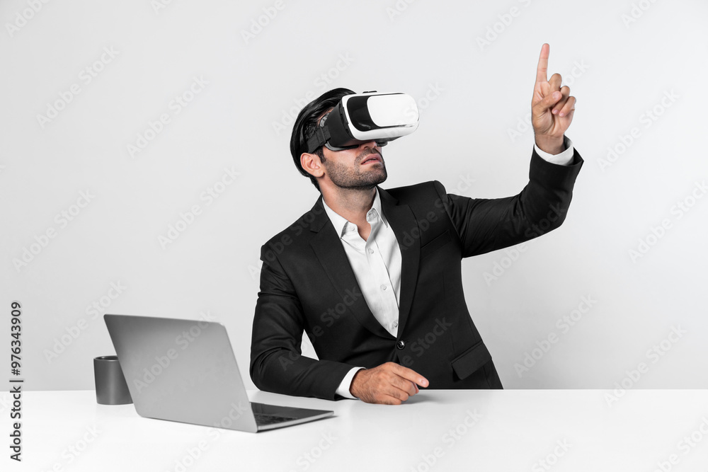 Skilled business man looking at data analysis while sitting at table with laptop and wearing VR glasses. Project manager working by using virtual reality system or connecting at metaverse. Deviation. Skilled business man looking at data analysis while sitting at table with laptop and wearing VR glasses. Project manager working by using virtual reality system or connecting at metaverse. Deviation.