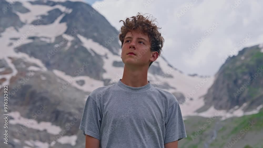 Portrait of Teenager curly boy in a T-shirt standing against snowy mountains Switzerland in summer Portrait of Teenager curly boy in a T-shirt standing against snowy mountains Switzerland in summer