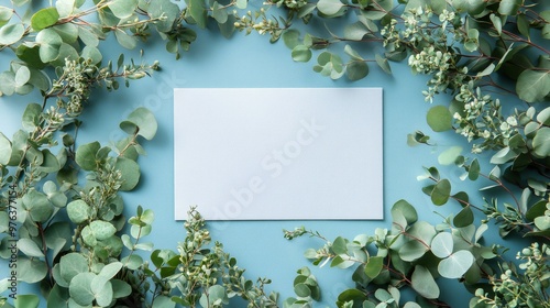Fresh green leaves arranged around a blank card on a light blue background