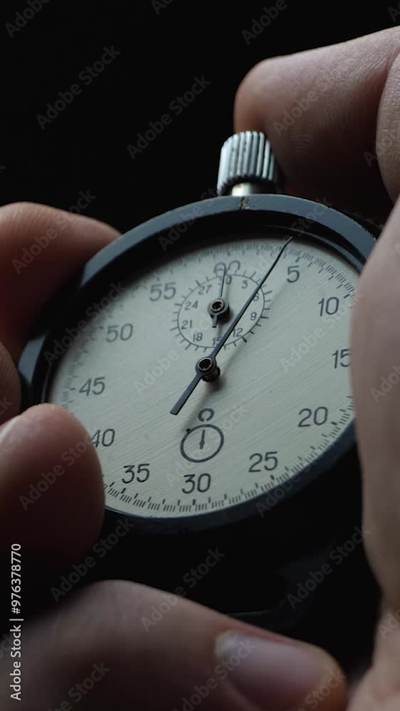 Black analogue stopwatch in hand on black background. Time start with old chronometer. Man presses start button. Sports or business concept, successful teamwork and counting down time