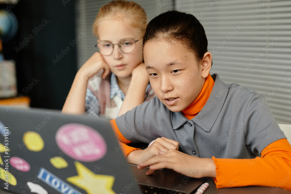 Portrait of concentrated Central Asian girl using laptop in class while browsing information and watching educational videos together with classmate at school, copy space Portrait of concentrated Central Asian girl using laptop in class while browsing information and watching educational videos together with classmate at school, copy space