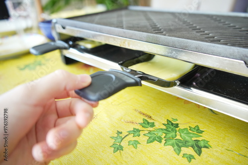 Hand inserting a piece of swiss raclette cheese in a melter, which is then put into a raclette Grill.  photo