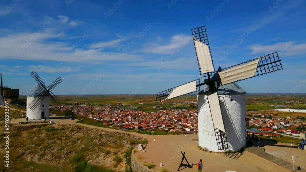 A wide view of a landscape with white windmills in the foreground and a town in the background under a blue sky, aerial view, Consuegra, Toledo, Castilla-La Mancha, Spain, Europe