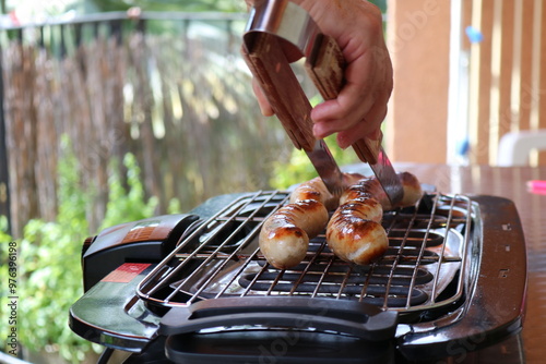 Person grilling bratwurst sausages on a barbecue grill outdoors.