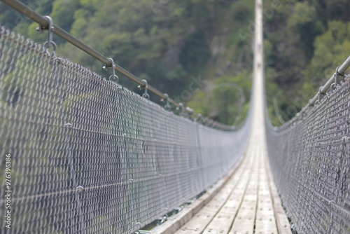 Suspension bridge with selective focus, showing wooden planks and ropes surrounded by nature.