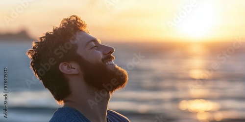 A person with curly hair and a beard enjoys the warm sunset by the sea, head tilted back, reveling in the serene moment of nature's beauty in the evening light. photo