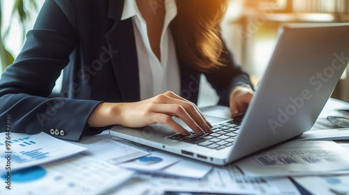 Thoughtful businesswoman typing on a laptop, documents scattered around her, representing hard work and strategy, serious mature businesswoman