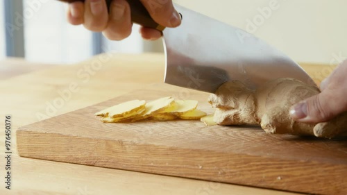 Close up of female hands slicing fresh ginger root on wooden cutting board