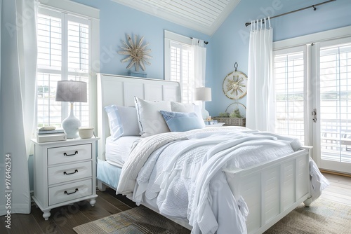 A white bed with a white bedspread and white pillows sits in a bedroom with blue walls and white shutters on the windows. A nightstand is next to the bed, and there are curtains on the window.