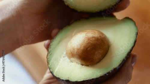 Female hands opening fresh ripe avocado at kitchen, close up