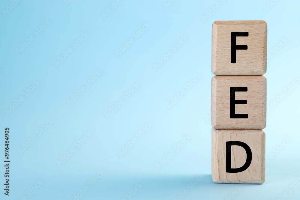 Stack of wooden cubes with letters Fed (Federal Reserve System) on light blue background, closeup. Space for text Stack of wooden cubes with letters Fed (Federal Reserve System) on light blue background, closeup. Space for text