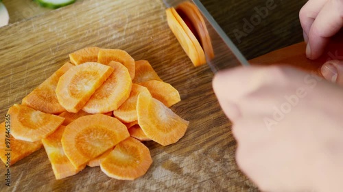Female hands slicing fresh carrot on cutting board, top view