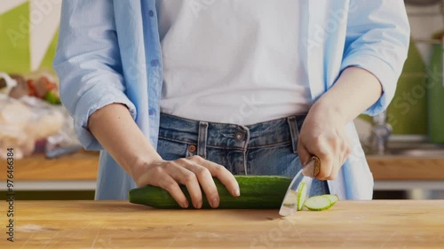 Professional chef slicing fresh cucumber on wooden cutting board at kitchen