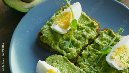 Healthy breakfast. Three toasts with smashed avocado, eggs and microgreens on plate, close up