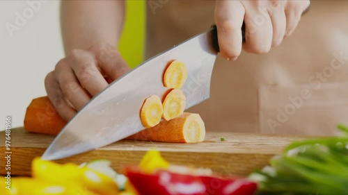 Woman cutting fresh orange carrot on kitchen board, preparing healthy dinner