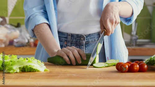 Woman cutting fresh cucumber for vegetable salad at kitchen