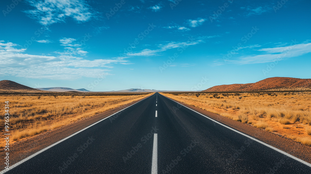 A long, straight highway stretches through a vast, arid desert under a clear blue sky, flanked by dry grass and distant hills. A long, straight highway stretches through a vast, arid desert under a clear blue sky, flanked by dry grass and distant hills.