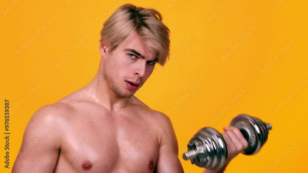 Muscular sportsman with naked body lifting dumbbell in hand, looking at camera seductively, orange studio background, slow motion Muscular sportsman with naked body lifting dumbbell in hand, looking at camera seductively, orange studio background, slow motion