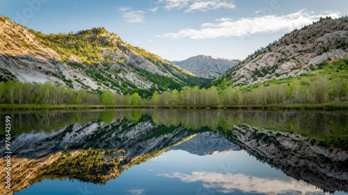A photo of a serene landscape with a calm lake reflecting the surrounding mountains, trees, and sky. The mountains have a rocky terrain with green vegetation. There are trees near the lake.