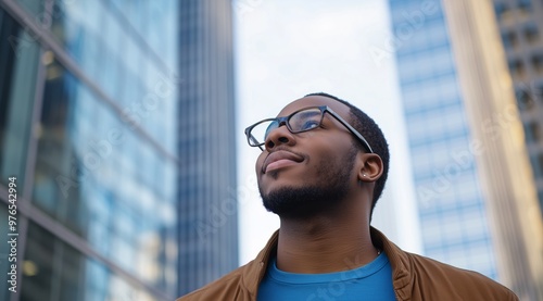 Man in Glasses Smiling and Looking Up Near Glass Building in Cityscape