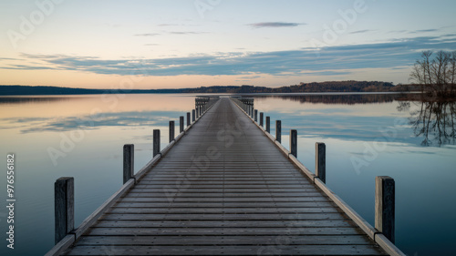 Wallpaper Mural A photo of a long, wooden pier extending into the calm, tranquil waters of a serene lake. The pier is lined with wooden posts. The sky is clear, with a few clouds, and the trees on the distant shore Torontodigital.ca