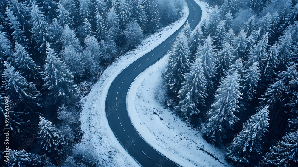 Aerial view of a snow-covered forest with a winding road cutting through, offering a scenic and peaceful winter scene.