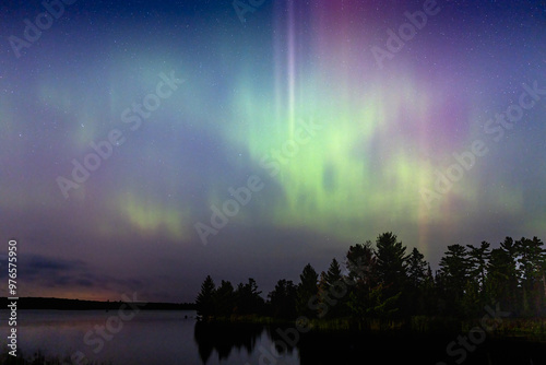 Northern lights erupt over remote Minnesota lake at night with rainbow of color shining off water Aurora Borealis nature show