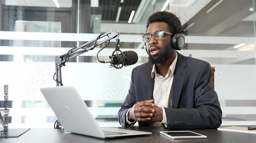 Wallpaper Mural African American businessman wearing headphones engaged in podcast. Using laptop and microphone he communicates ideas in modern office environment. Concept of media, business communication, technology Torontodigital.ca