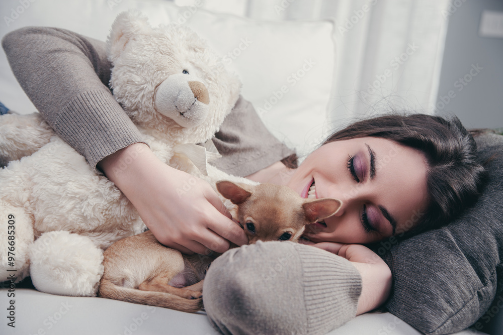 Happy young woman relaxing on sofa with puppy and teddy bear