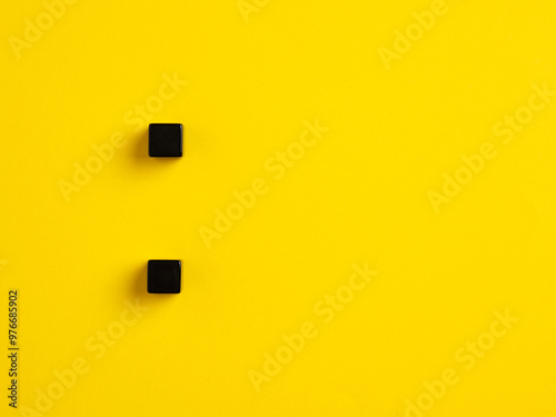 The colon symbol punctuation mark. Two black cubes on yellow background.