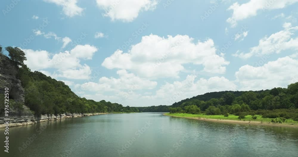 River flowing between green hills under a bright blue sky with scattered white clouds River flowing between green hills under a bright blue sky with scattered white clouds