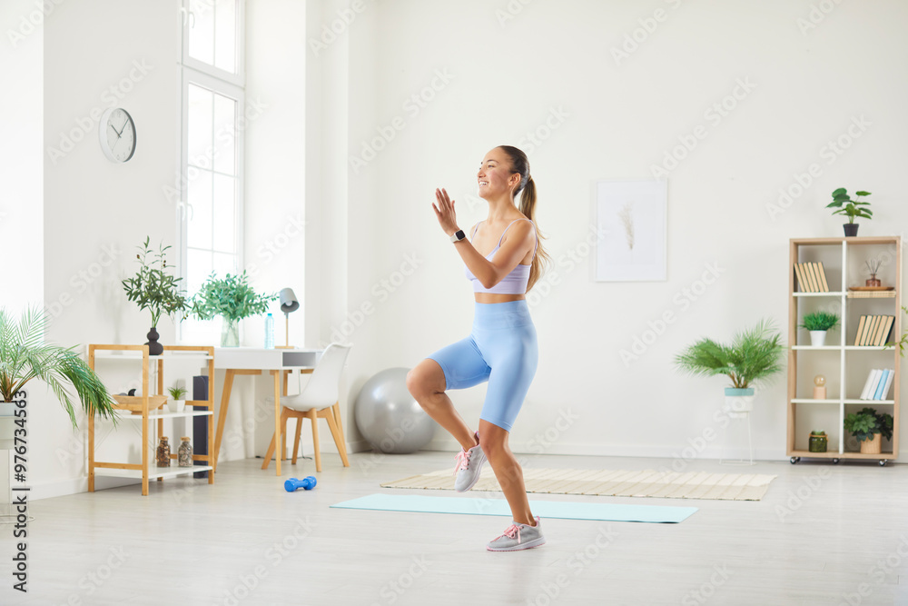Happy beautiful sporty young Asian woman in sportswear doing a jumping and running in place exercise with high knee raises during her fitness workout in the living room at home