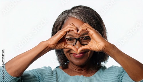 Mature woman wears eyeglasses looking at camera through joined fingers showing heart symbol,