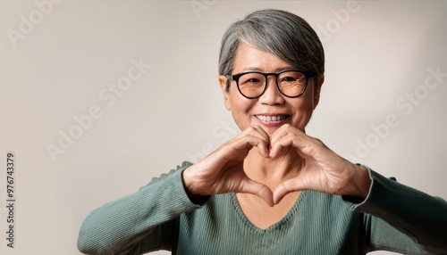 Mature woman wears eyeglasses looking at camera through joined fingers showing heart symbol,