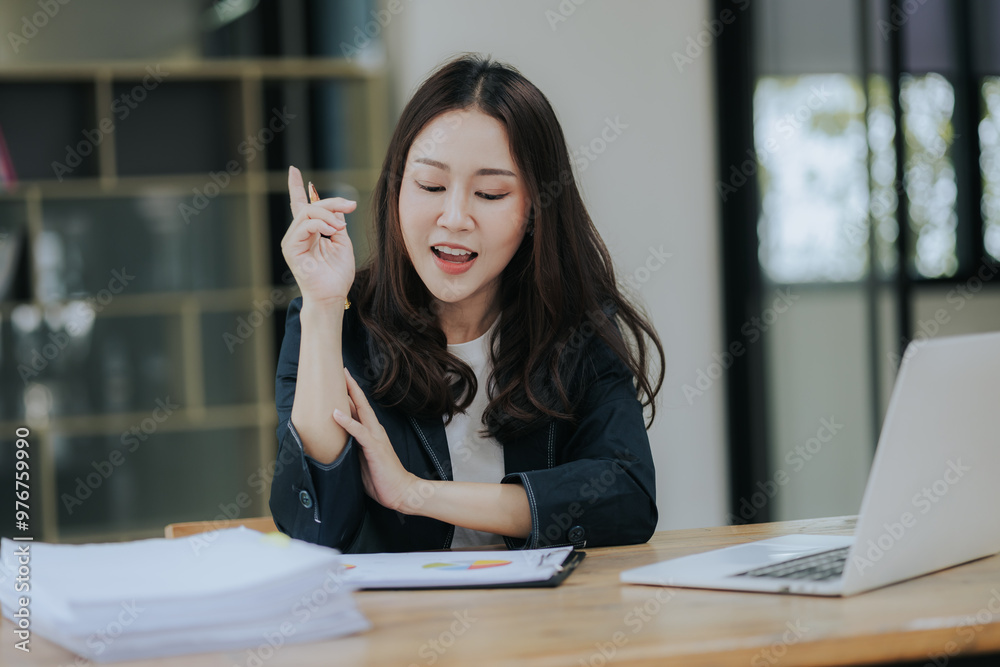 A cheerful young Asian businesswoman sits at her modern desk, typing on a laptop, working on corporate projects with paperwork, smiling in a busy workplace. A cheerful young Asian businesswoman sits at her modern desk, typing on a laptop, working on corporate projects with paperwork, smiling in a busy workplace.