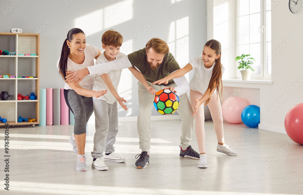 Fototapeta premium Family with children playing an active game with ball, during training in the gym, exercising and having a time together. Happy faces reflect the joy of being active and spending quality time.