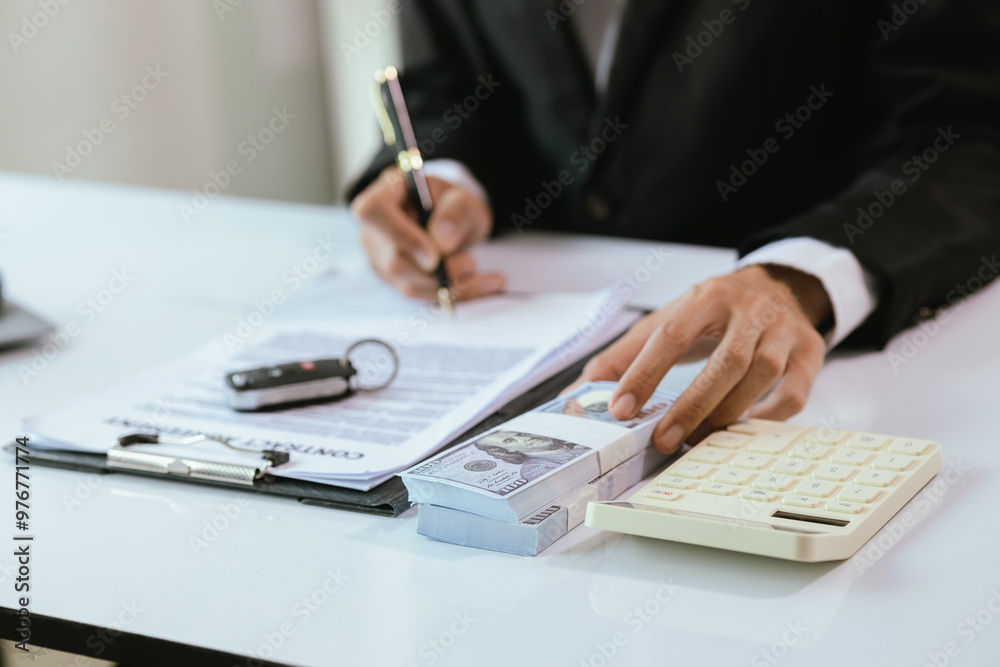 Naklejka premium A satisfied customer signs paperwork at a car dealership, finalizing the purchase of a new vehicle. The salesman hands over the car key, completing the finance and insurance deal.