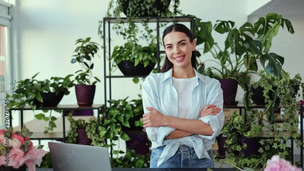 A happy and friendly young female florist stands in her flower shop surrounded by plants and flowers. She smiles warmly at the camera, exuding confidence and passion for her business. A happy and friendly young female florist stands in her flower shop surrounded by plants and flowers. She smiles warmly at the camera, exuding confidence and passion for her business.