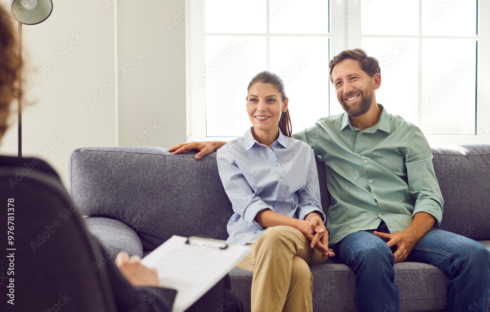 Young smiling couple sitting on sofa and talking with psychologist trying to find problems and solution at counselor's office. Family therapy, relationship and mental health concept. Young smiling couple sitting on sofa and talking with psychologist trying to find problems and solution at counselor's office. Family therapy, relationship and mental health concept.