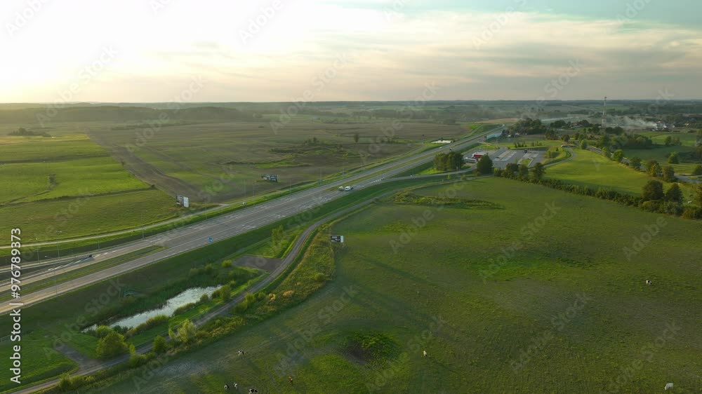 Serene aerial view of highway curving through green fields at sunset
