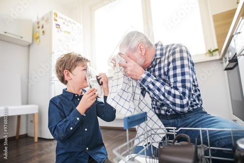 Boy helping grandfather clean the kitchen, unloading clean dishes out of the dishwasher. Grandfather taking care of grandson while parents are at work.