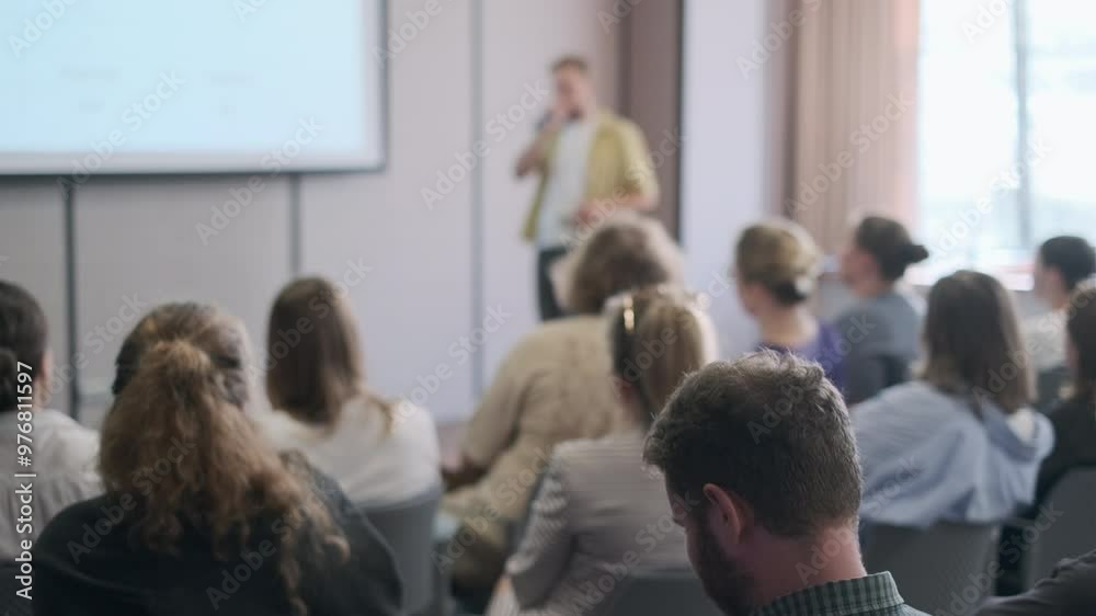 Group of people attentively listening to a speaker during a business seminar in a modern conference room.