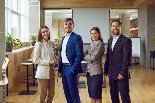 Portrait of a happy young business people men and women looking at camera and smiling indoors. Company employees or group of staff standing in office in suits confidently and cheerfully. photo