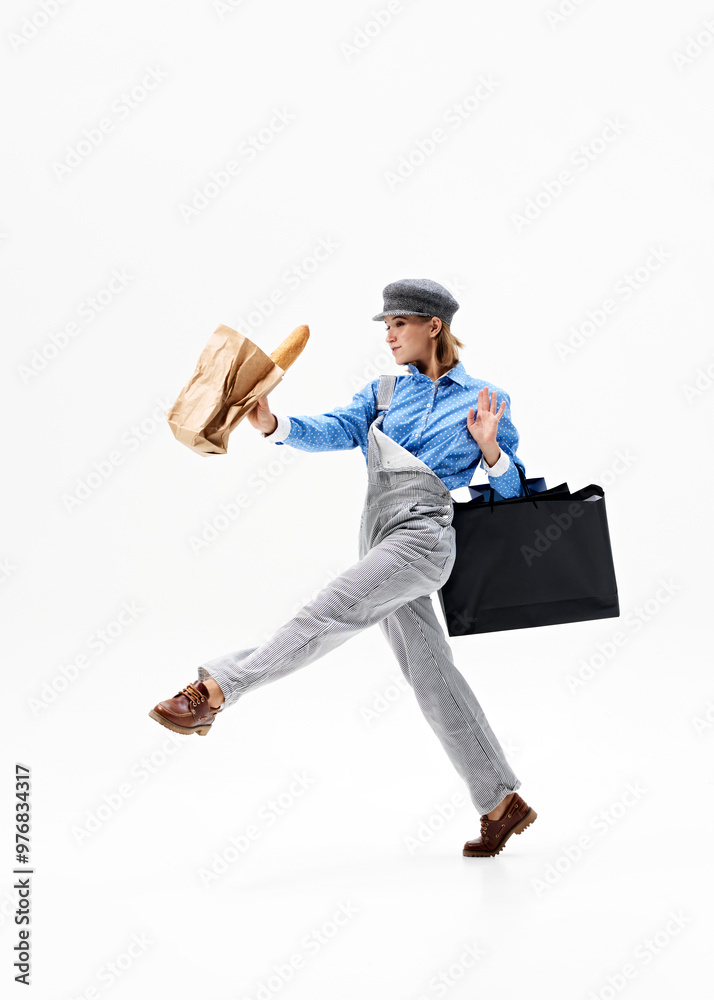 With one arm confidently holding shopping bags and carefully carrying baguette against white background, mixing fashion and function in stylish walk. Concept of shopping, Black Friday, sale season. Ad With one arm confidently holding shopping bags and carefully carrying baguette against white background, mixing fashion and function in stylish walk. Concept of shopping, Black Friday, sale season. Ad