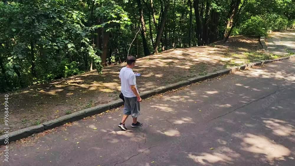 A teenager in shorts with headphones and a phone walks through the park in summer A teenager in shorts with headphones and a phone walks through the park in summer