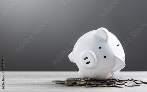 White piggy bank and a pile of coins on a wooden table against a grey background, with ample copy space for text. The image symbolizes savings, financial planning, and responsible money management. photo